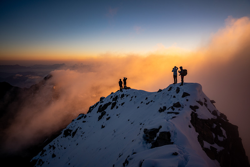 白雪皑皑的山顶上，日出时徒步者的剪影图片素材