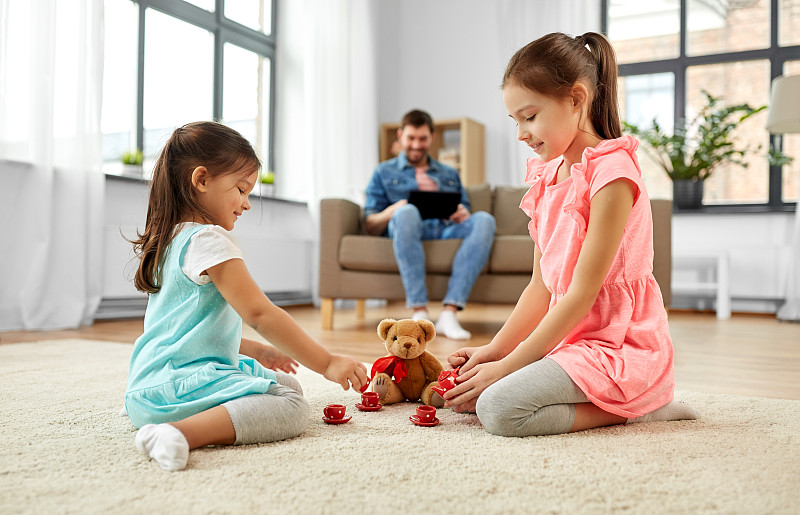 童年，休闲和家庭概念-小姐妹们在家里玩茶会游戏，玩具陶器和泰迪熊。女孩们在家里玩玩具陶器和泰迪熊图片素材