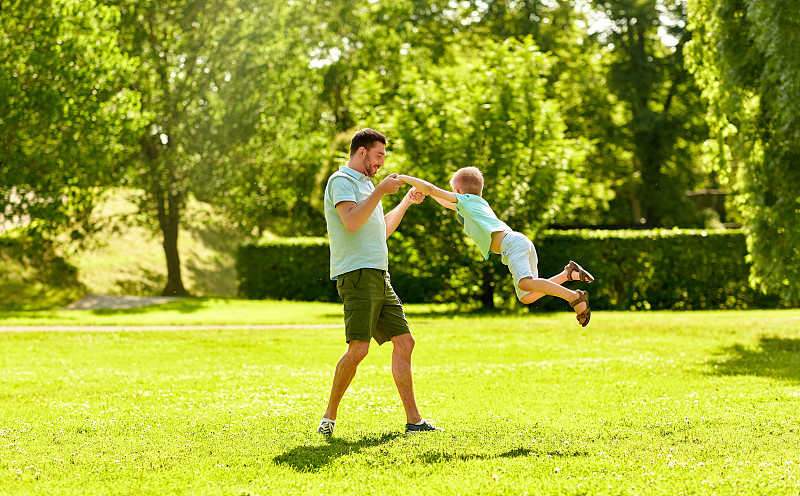 家庭、休闲、人的概念——快乐的父亲和小儿子在夏日公园玩耍。快乐的父亲和儿子在夏季公园玩图片下载