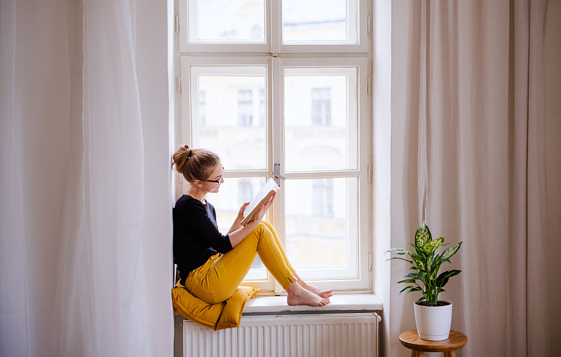 一个拿着书坐在窗台上学习的年轻女学生图片素材