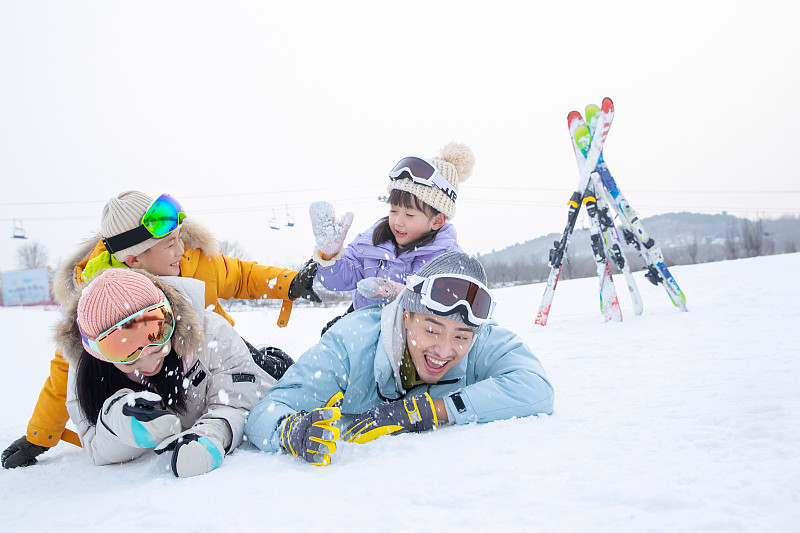 快乐的一家四口趴在雪地上打雪仗图片下载