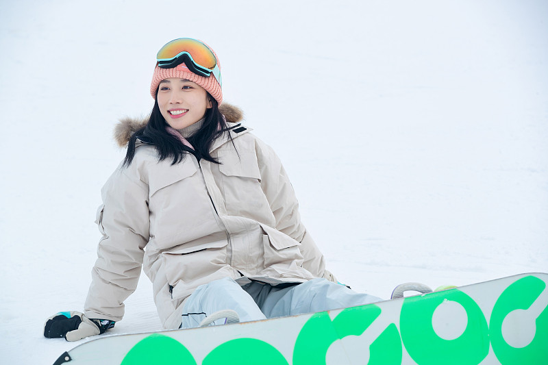 踩着单板坐在雪地上的青年女人图片下载