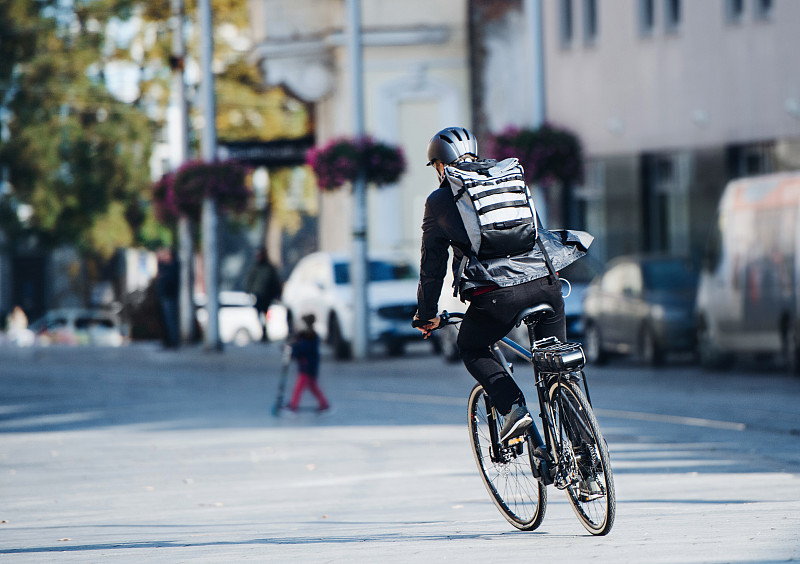 男性自行车快递员在城市复印空间投递包裹的后视图图片素材