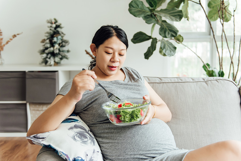 一位亚洲孕妇正在吃绿色的蔬菜图片素材