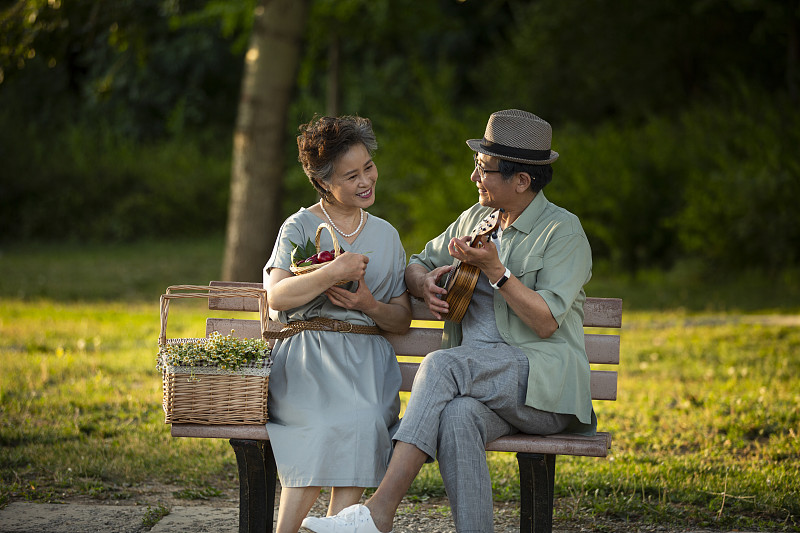 浪漫的老年夫妻坐在公园长椅上野餐弹奏尤克里里琴图片下载