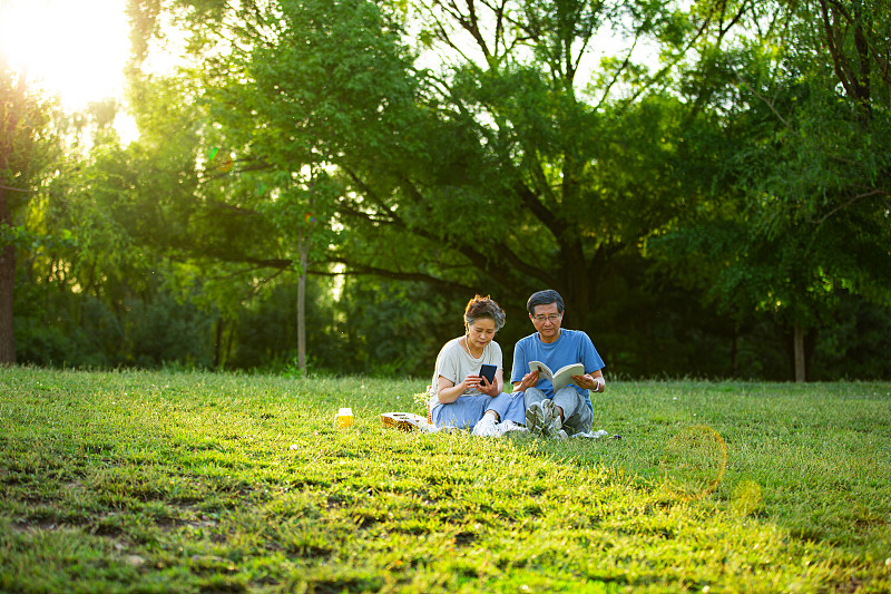 老年夫妻在户外公园野餐看书看手机图片素材