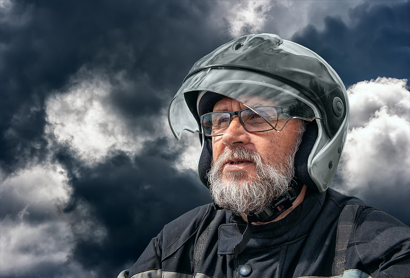 多云的天空中骑摩托车的老人的肖像图片素材