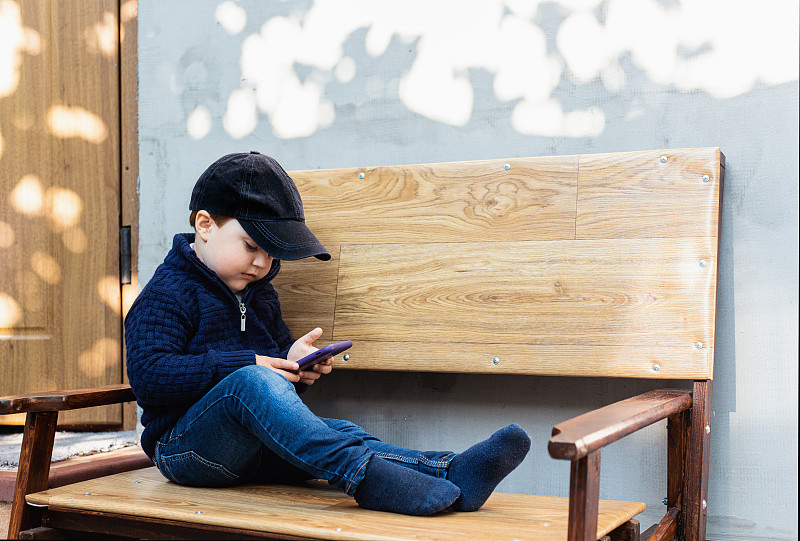 乌克兰敖德萨，坐在户外木凳上玩手机的男孩图片素材