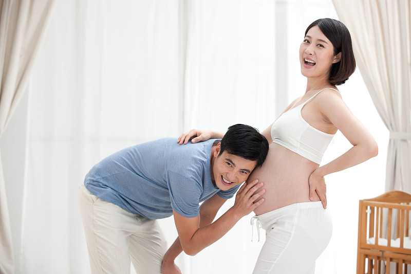年轻父亲抚摸孕妇的肚子聆听胎儿图片下载