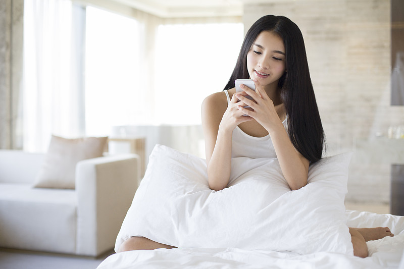 年轻女子在床上玩手机图片下载