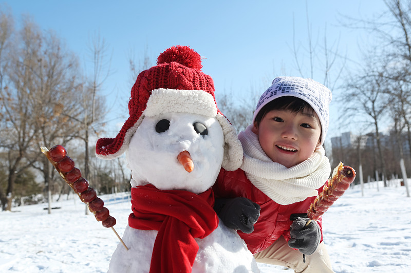 男孩拿着糖葫芦和雪人在雪地上图片素材