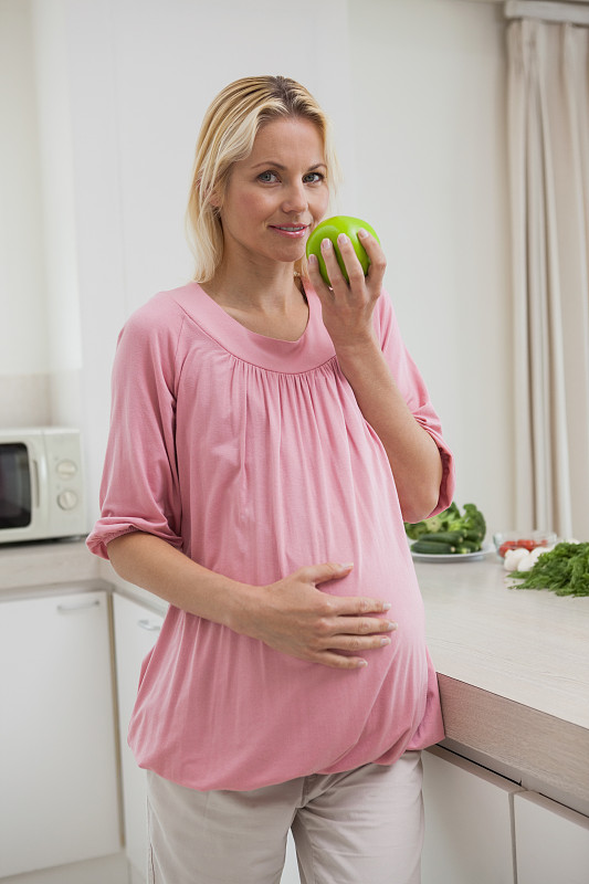 一个孕妇在厨房里拿着苹果的肖像图片素材