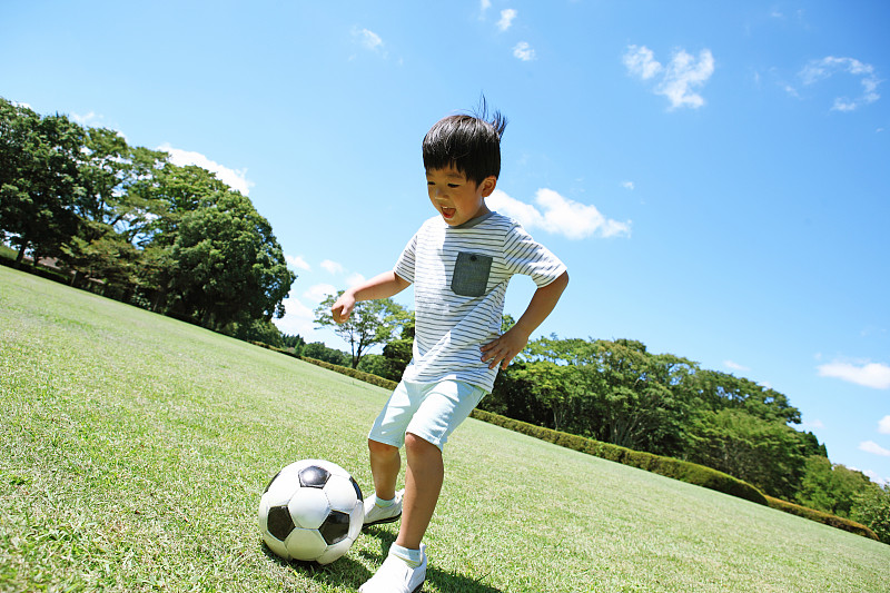 一个日本小男孩在城市公园踢足球图片下载