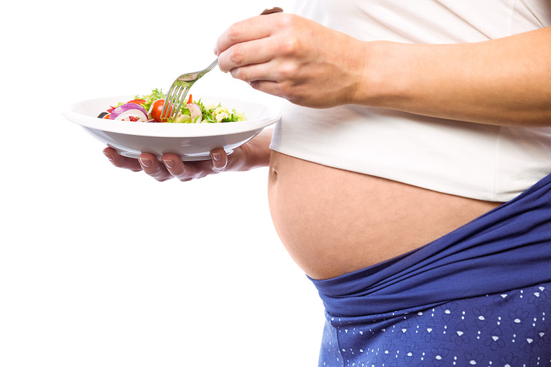 一名孕妇在白色背景下吃沙拉图片下载