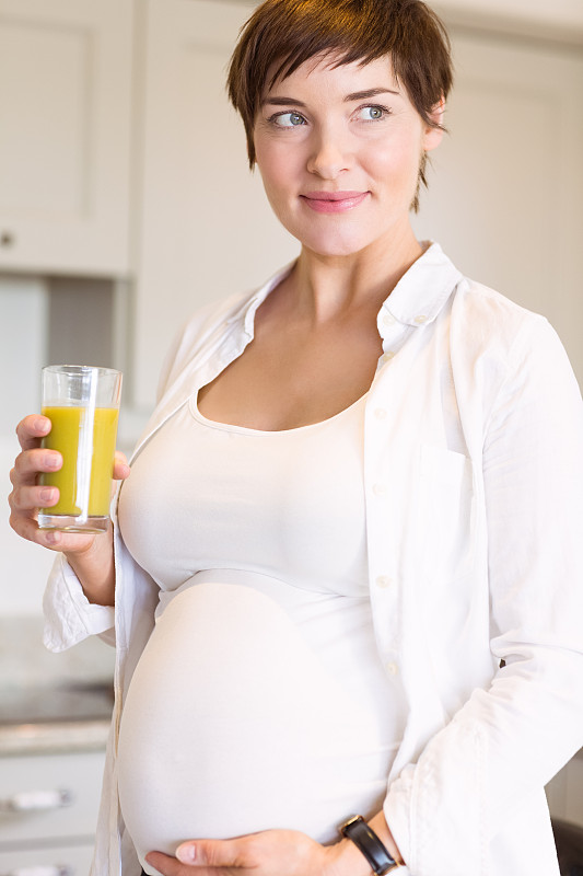 孕妇在家厨房里喝着橙汁图片素材