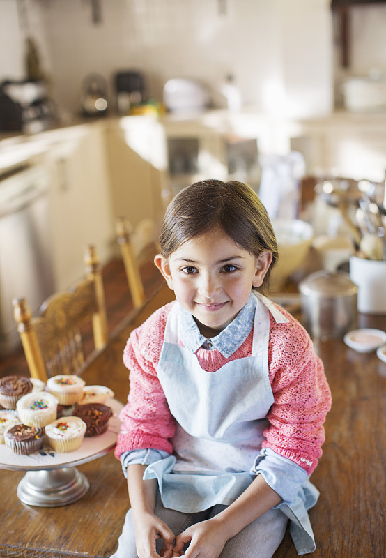 小女孩坐在厨房桌子上，旁边是纸杯蛋糕图片下载