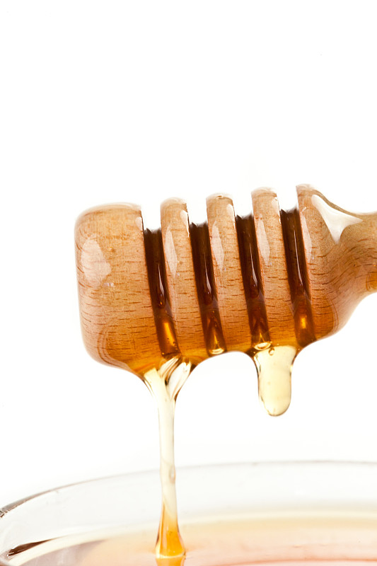 在白色的背景下，蜂蜜滴落在装满蜂蜜的碗的顶部图片素材