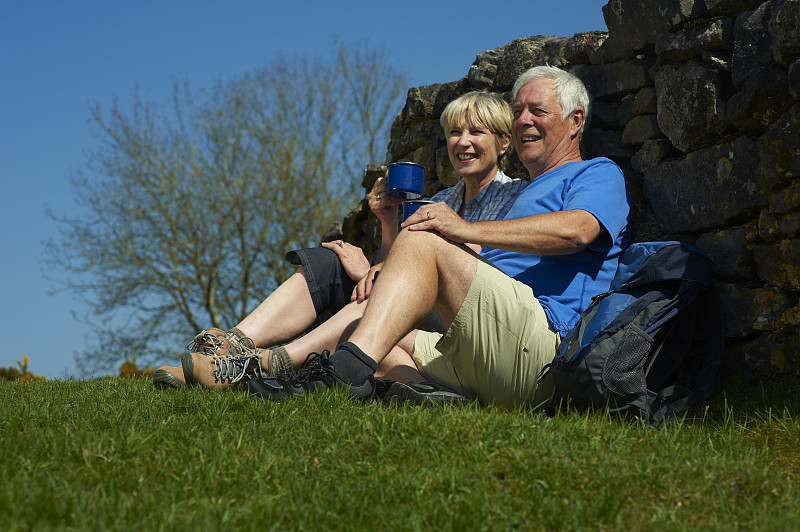 一对退休夫妇靠在鹅卵石墙上休息图片下载