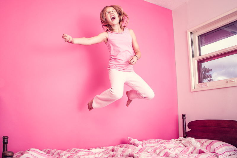 女孩在粉红色的房间的床上跳图片下载