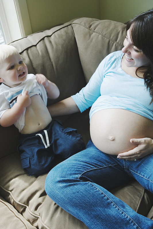 孕妇和儿子(2-4人)坐在沙发上，男孩撩起衬衫图片下载