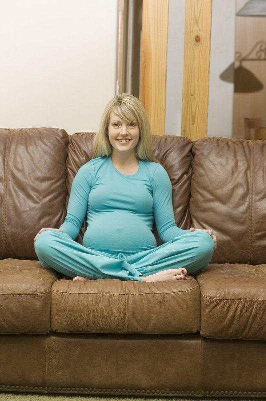 年轻孕妇双腿交叉坐在沙发上，画像图片下载