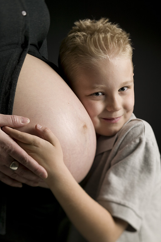 男孩(4-5)把耳朵贴在孕妇的肚子上，肖像图片下载