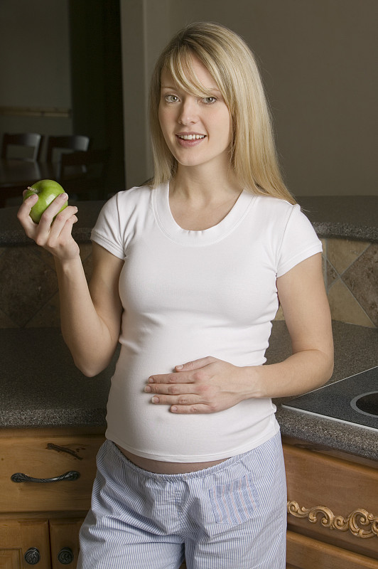 孕妇在厨房拿着苹果，肖像图片下载