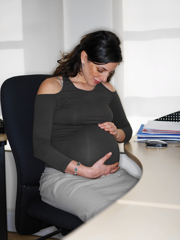 年轻孕妇抱着肚子坐在办公桌前图片下载