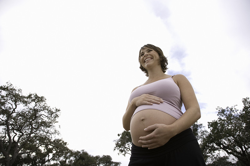 孕妇双手放在腹部，面带微笑，低角度拍摄图片下载