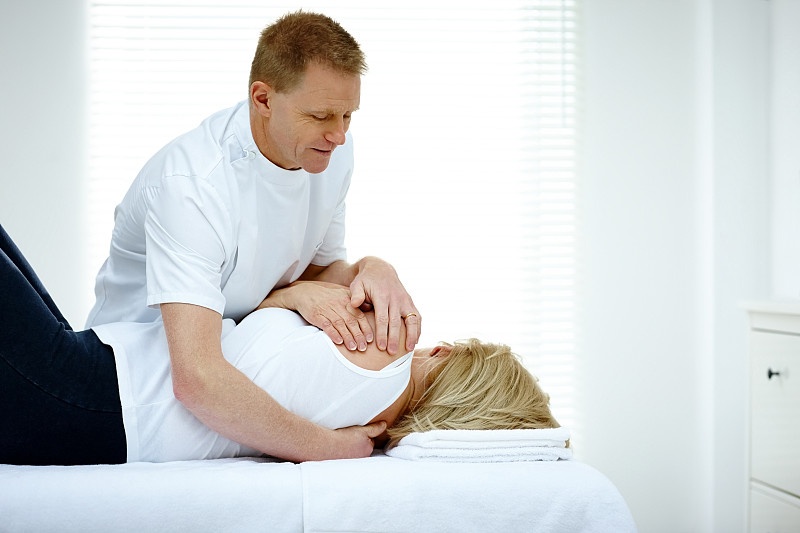 一位男性理疗师在按摩一位年长女性的背部图片下载