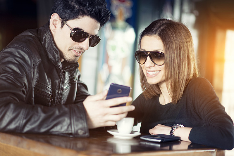 一对情侣在咖啡馆里用手机微笑图片下载