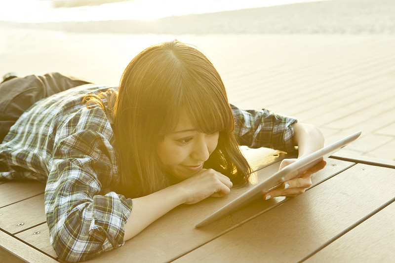 年轻女子躺在沙滩上用着平板电脑图片下载