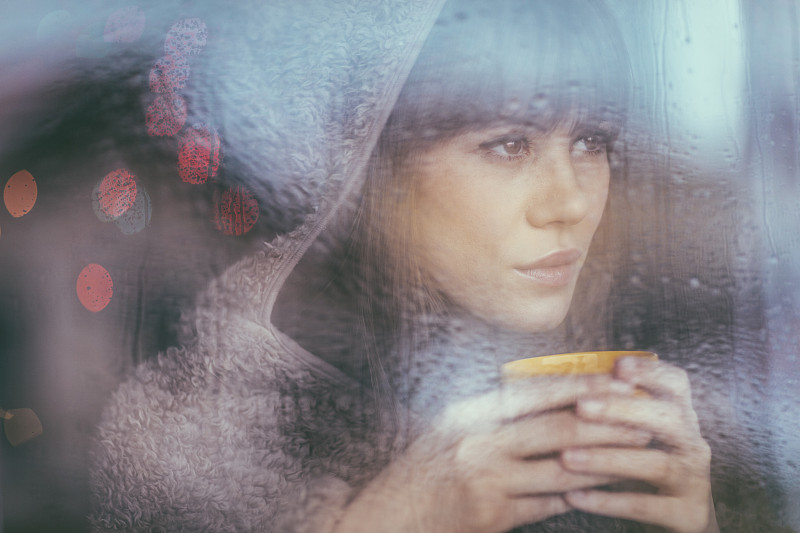一个年轻女子在雨天透过窗户看图片下载