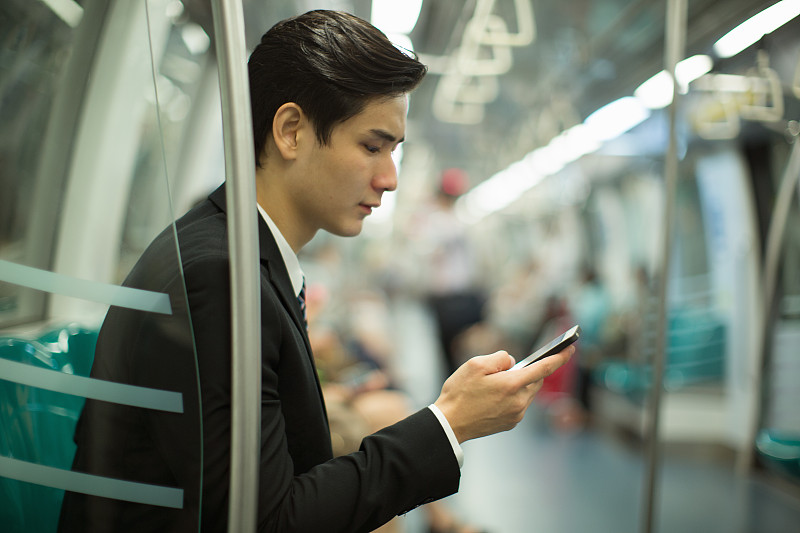 一个坐在地铁里看手机的年轻人。图片下载