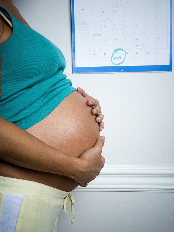 一个孕妇在日历前触摸她的肚子的侧面图片下载
