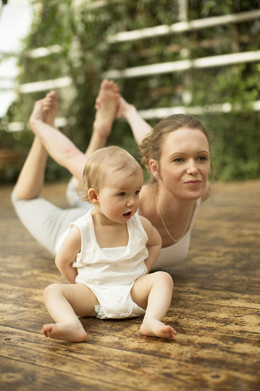 妇女做瑜伽锻炼，而婴儿坐在旁边图片下载