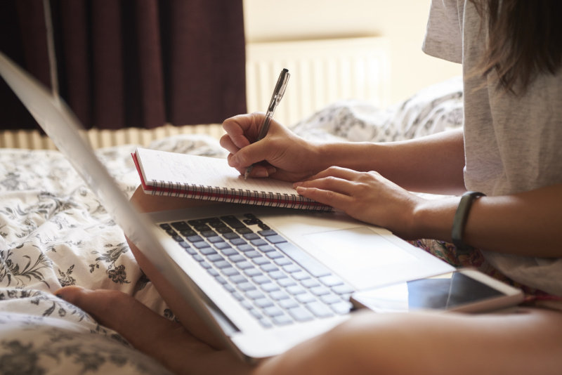 一个女人坐在床上使用笔记本电脑的特写图片下载