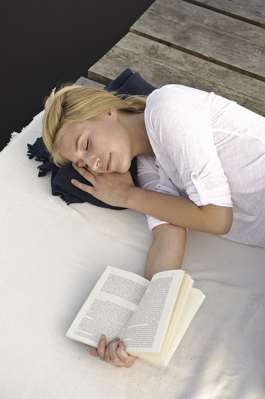 年轻女子躺在毯子上看书图片下载