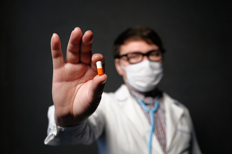 一名亚洲医生穿着长袍，戴着医用口罩，手里拿着一粒药丸。预防和治疗病毒和流感、肺炎暴发和冠状病毒流行的概念。图片素材