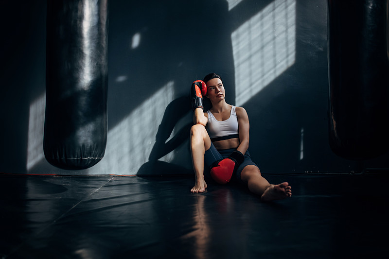 疲惫的年轻女子拳击手坐在地板后，练习和休息图片下载