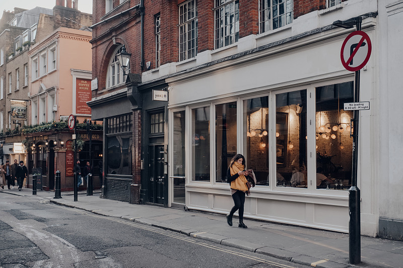 在英国伦敦苏荷区，一排咖啡馆和餐馆，女人走过，运动模糊。图片下载
