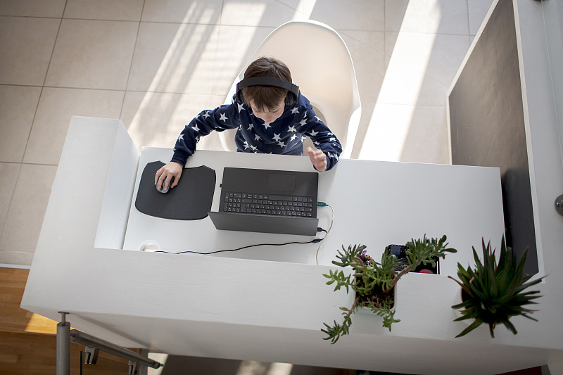 俯视图男孩坐在家里的书桌上戴着耳机和使用笔记本电脑图片下载
