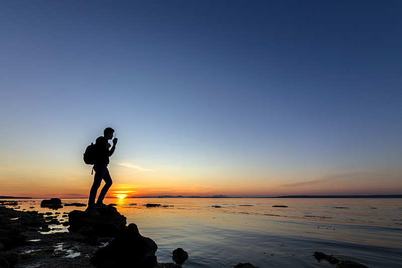 一个拿着步话机的人站在海边的岩石上图片素材