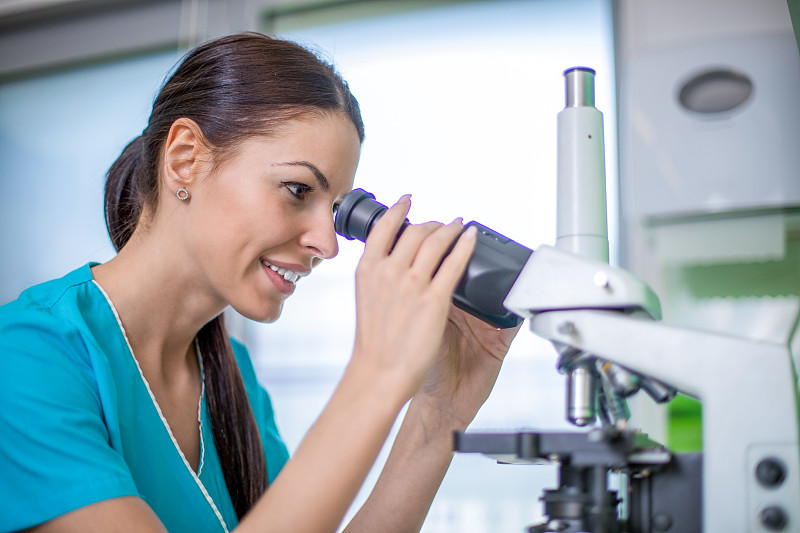 在实验室里研究显微镜的年轻女化学家。图片素材