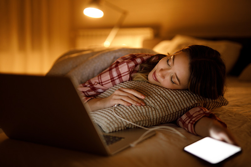 一名年轻女子在家里的笔记本电脑前睡在自己的床上图片素材