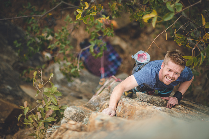 年轻的男性攀岩者正爬上岩壁，抬头看着镜头图片素材