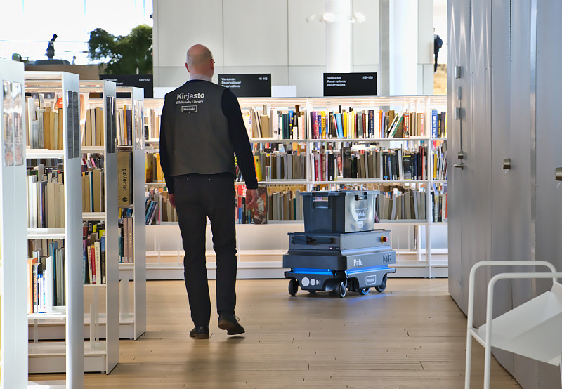 一名图书馆员工在跟着一个运输机器人的移动图片素材