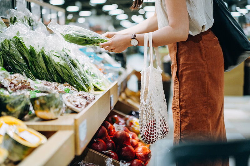 年轻的亚洲妇女在超市购买新鲜的有机食品杂货的镜头。她正用一个棉网环保袋购物，里面装着各种水果和蔬菜。“零浪费”的概念图片素材