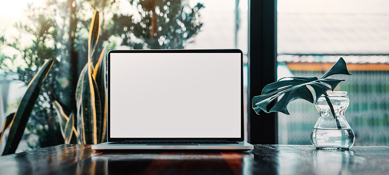 笔记本电脑空白屏幕上的桌子在咖啡馆的背景。笔记本电脑与空白屏幕上的咖啡店模糊背景。图片下载
