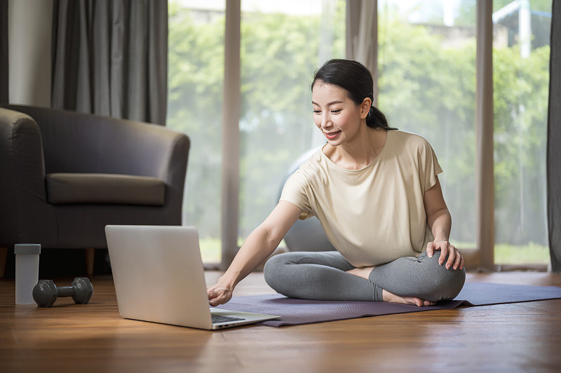 一个女人在家里用笔记本电脑做瑜伽，在网上找到锻炼教程。家庭隔离期间的家庭健身直播。健康的生活方式和工作生活的平衡理念。图片下载